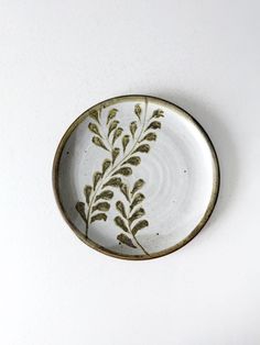 a small white plate with green leaves on the rim, against a white wall background