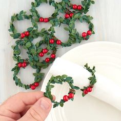 a hand holding a napkin over a plate with holly wreaths on it and red berries