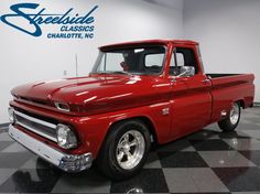 an old red pickup truck is parked in a showroom with black and white checkered flooring