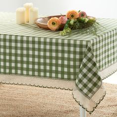 a green and white checkered table cloth with flowers on it, next to candles