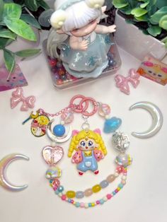 an assortment of charms and necklaces on a table next to some plant life in the background