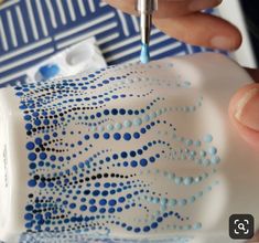 a person is using a pen to draw dots on a white and blue object with black spots