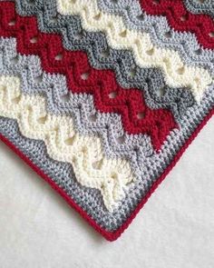 a crocheted blanket with red, white and grey squares on it's edges