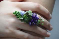 a woman's hand holding a ring with purple flowers on it and green leaves