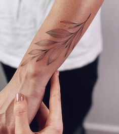 two hands holding each other with a tattoo on the wrist and arm, both showing leaves