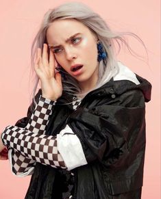 a woman with grey hair is holding her hand up to her face while wearing black and white checkered jacket