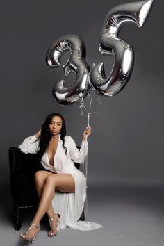 a woman sitting on a chair holding balloons in front of her face and the number 55