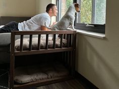 a man laying on top of a bed next to a dog looking out the window