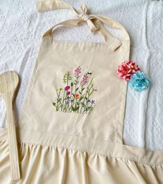 a white apron with flowers on it next to a wooden spoon and flower pot holder