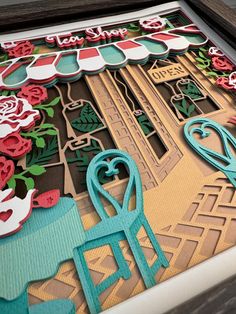 a close up of a table with paper cut outs and flowers on the top, in front of a wooden frame