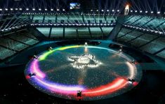 the olympic rings are lit up at night in front of an arena full of spectators