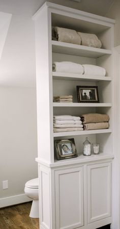 a white bookcase with folded towels on top of it next to a toilet in a bathroom