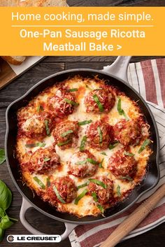 a skillet filled with meatballs and cheese on top of a table next to bread