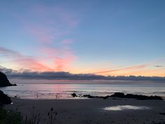 the sun is setting at the beach with rocks in the foreground and clouds in the background