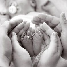 a black and white photo of a baby's feet being held by two adults