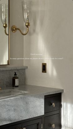 a bathroom vanity with marble counter top and gold faucet light fixture over it