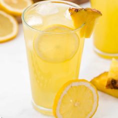 a glass filled with lemonade next to sliced pineapples on a white table