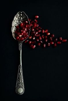 a spoon filled with pomegranate on top of a black table next to it