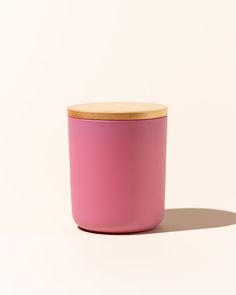 a pink container with a wooden lid on a white surface, against a plain background