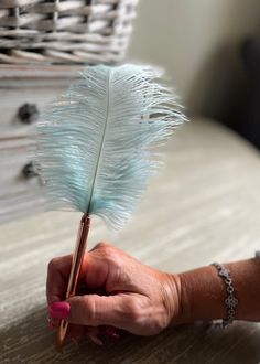 a person holding a feather on top of a wooden table next to a stack of books