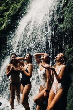 three beautiful women in bathing suits standing next to a waterfall