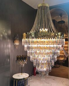 a woman standing next to a chandelier in a room with mirrors on the wall