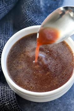 a spoon pouring sauce into a white bowl on top of a blue cloth with a black towel in the background