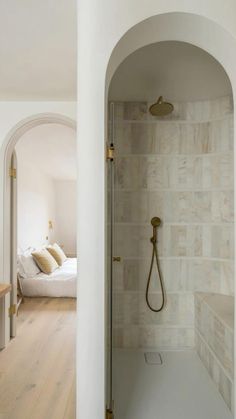 an arched doorway leads to a bedroom with a bed in the background and a shower head