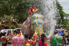 an elephant spraying people with water on it's back and its face covered in colorful paint