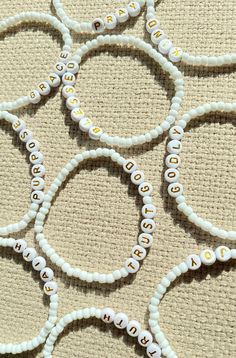 several white beads with gold letters are arranged on a beige surface and the word love is spelled in cursive writing