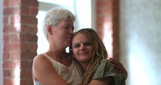 two women embracing each other in front of a brick wall and window with sunlight streaming through the windows