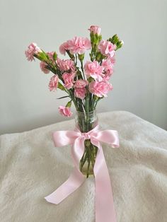 pink carnations in a vase tied with a pink ribbon on a white blanket