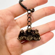 a hand holding a keychain with two cats on it's back and one cat hanging from the chain