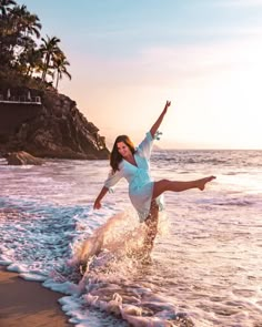 a woman is dancing on the beach with her feet in the air and arms out