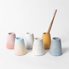 five different colored vases with a toothbrush in them