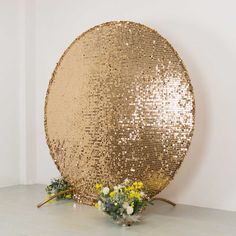 a large gold sequin covered plate sitting on top of a table next to flowers