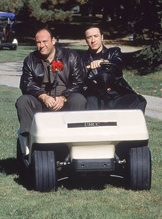 two men in leather jackets are sitting on a golf cart and one is holding a flower