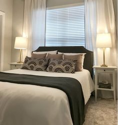 a bed sitting under a window with two lamps on either side of the headboard