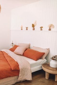 a bed with orange sheets and pillows in a white room next to a wooden table