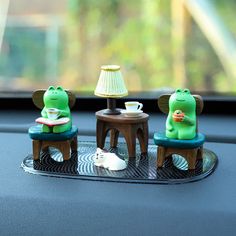 three toy frogs sitting on small stools in the dashboard of a car with a lamp