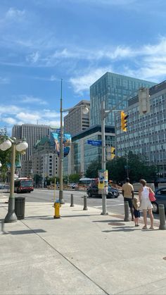 people are standing on the sidewalk in front of some tall buildings and traffic light poles