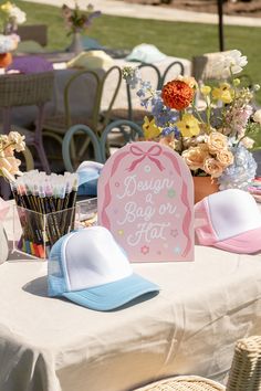 a table topped with hats and flowers on top of a white cloth covered tablecloth