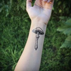 a mushroom tattoo on the wrist is shown in black and white ink, with a knife sticking out of it