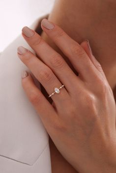 a woman's hand with a diamond ring on her left hand, wearing a white shirt