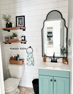 a white toilet sitting next to a bathroom sink under a mirror on top of a wooden shelf