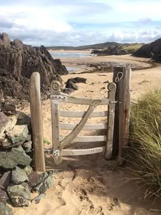 an old wooden gate on the beach with grass and rocks in the sand behind it