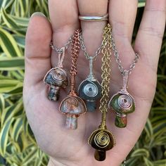 a person holding five different pendants in their hand with plants behind them on the other side