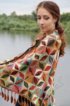 a woman wearing a multicolored crocheted shawl standing by the water