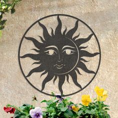 a sun face on the side of a building with flowers in front and behind it