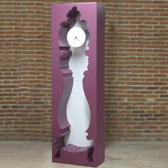 a tall purple and white clock sitting in front of a brick wall on the floor